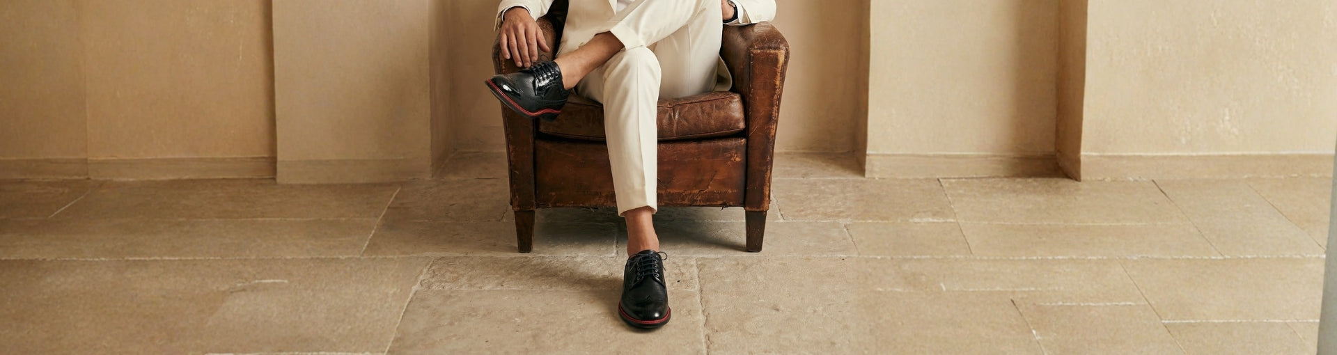 Man in beige suit seated wearing Pintta Dublin Black shoes, highlighting relaxed posture and quiet luxury footwear